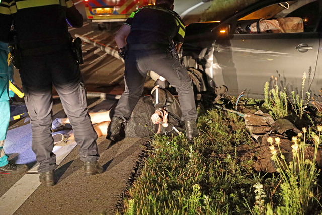 Agressieve automobilist rijdt lantaarnpaal uit de grond en wordt geboeid afgevoerd met ambulance