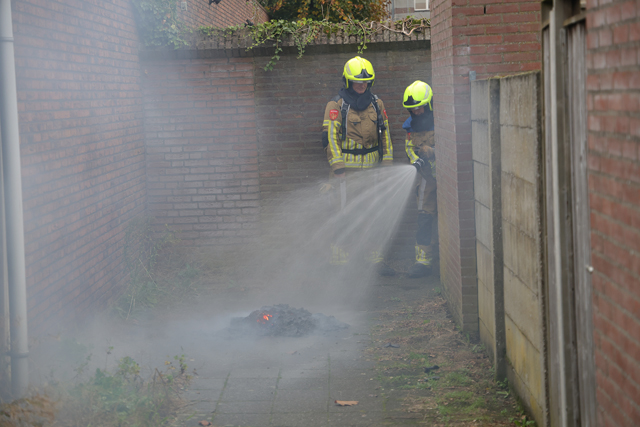Berg papier in brand in brandgang aan de Drogerij Waalwijk